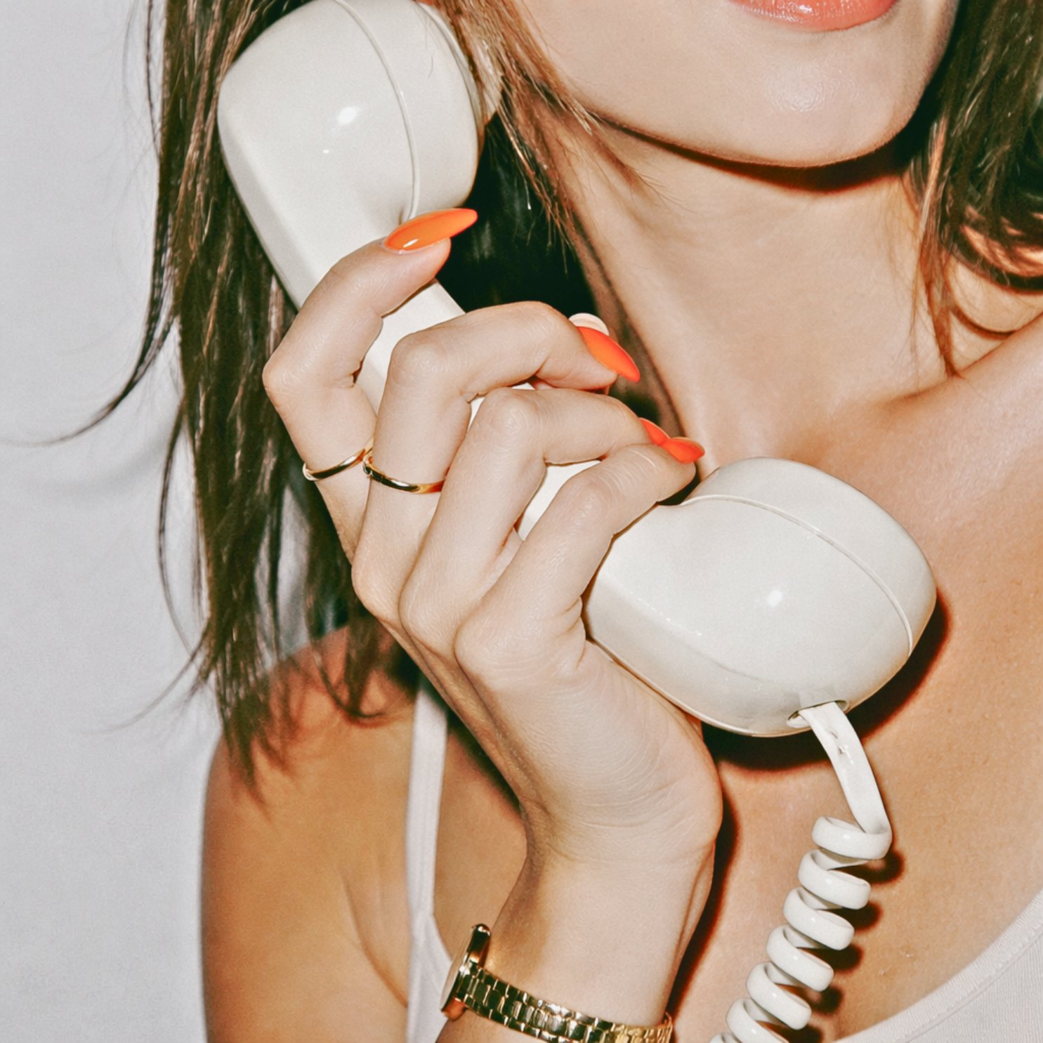 Woman holding two cream retro phone receivers with orange nails