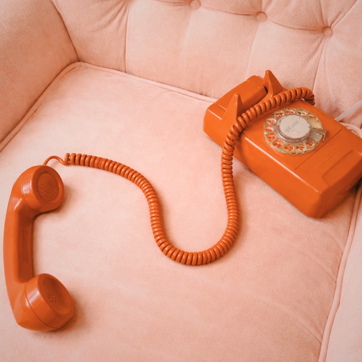 Vintage orange rotary phone on pink velvet chair
